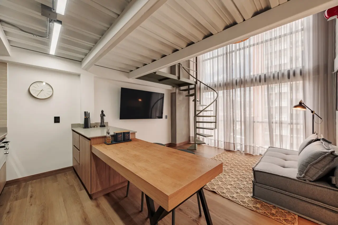 Centro Loft — the open lower floor: dining table, kitchen counter and the spiral stair up to the mezzanine, Centro, Medellín