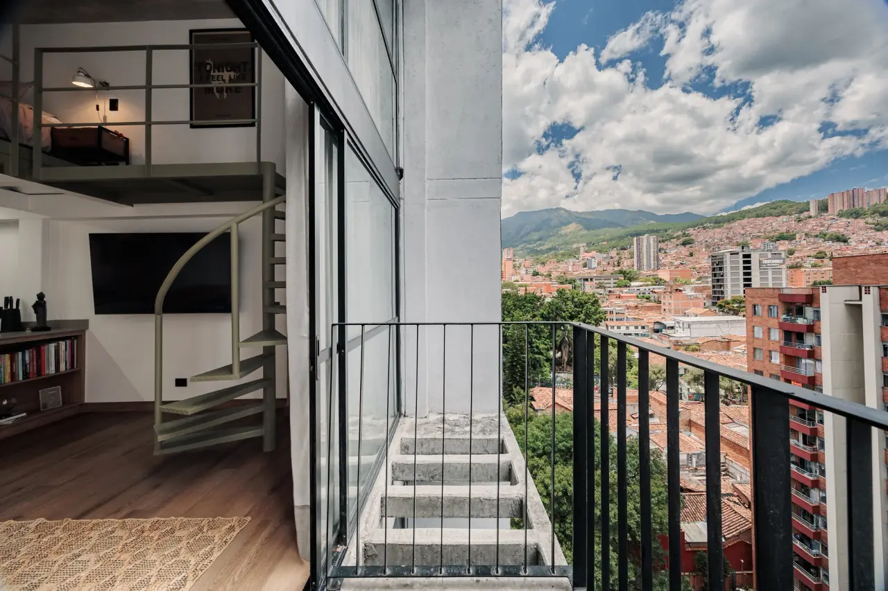 The private balcony at Centro Loft, with the spiral stair and central Medellín beyond the glass
